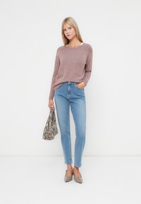 Lys rosa strikkegenser, høyhalsede blå jeans, grå spisse leppestifter, og en mønstret grå slangemønster håndveske.