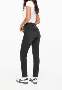 Vaqueros negros de mezclilla de tiro alto con un corte ajustado, cinco bolsillos y un ligero desgaste, combinados con zapatos blancos con detalles en negro.