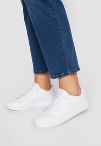 Vita sneakers med en slät yta, rund tå, snörningsdesign och en subtil logotyp. Kombinerat med avklippta denimjeans.