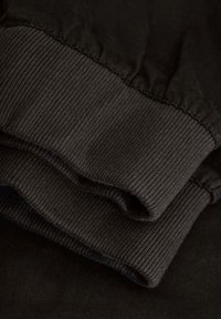 Černá bavlněná látka s elastickými žebrovými manžetami, úhledně složená. Textura vypadá hladce s mírným leskem, minimální švy jsou viditelné.