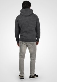 Sudadera gris oscuro con un tejido texturizado, diseño ajustado, capucha grande y puños acanalados, combinada con jeans gris claro y zapatillas negras.