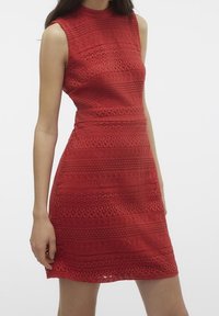 Punainen hihaton mekko, jossa on teksturoitu, kuvioitu neulekangas. Tiukka siluetti, polvipituinen, pyöreä pääntie ja näkyvät ommeltyöt.