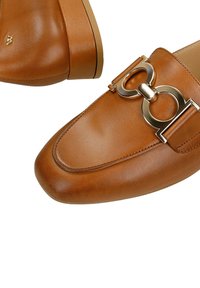 Mocassins en cuir marron avec détail boucle mors dorée et petit talon empilé sur fond blanc.