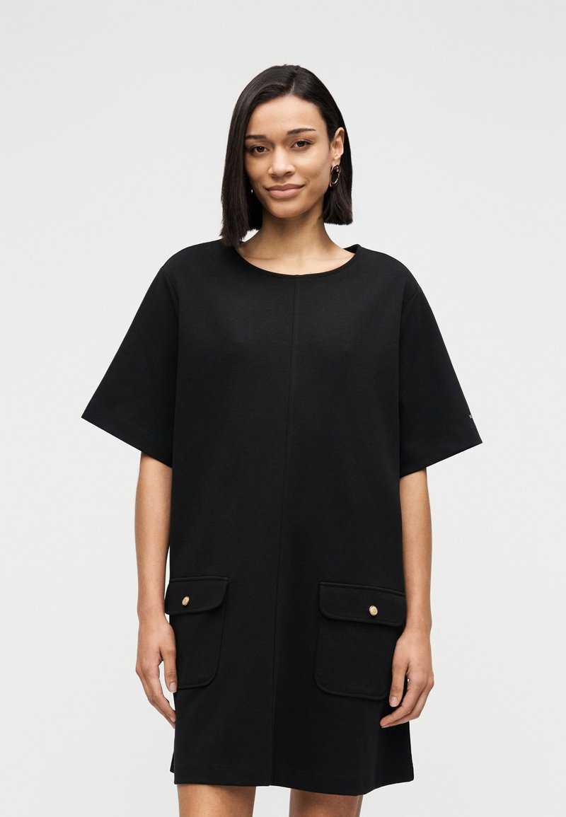 Μαύρο φόρεμα με κοντά μανίκια από μαλακό υλικό, με στρογγυλή λαιμόκοψη και δύο εμπρόσθιες τσέπες με χρυσές λεπτομέρειες.