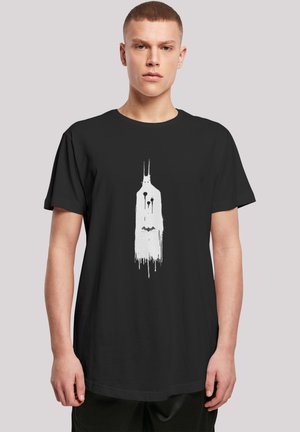 Svart t-skjorte med en hvit grafikk av en dryppende, stilisert figur med forlengede trekk, satt mot en nøytral bakgrunn.