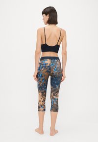 Fekete sportmelltartó vékony pántokkal, összeillő, kék, barna és natúr színű, batikolt mintás cropped leggings-t viselve; sima, rugalmas anyag.
