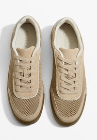 Beige színű sportcipők hálós és bőr felsőrésszel, kerek orral, fűzős kialakítással, párnázott bokapánttal és gumitalppal. Texturált felület világos részletekkel.