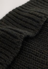 Knit black wool fabric with a textured, ribbed pattern. The edge is slightly folded, revealing a thick, soft texture.