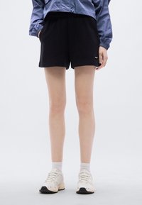 Μαύρα βαμβακερά σορτς με ελαστική μέση και ίσιο τελείωμα. Συνδυασμένα με λευκά αθλητικά παπούτσια και κάλτσες αστραγάλου. Απλός, καθημερινός σχεδιασμός.