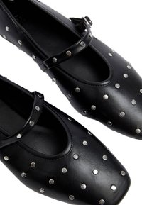 Ballerine in pelle nera con dettagli di borchie argentate decorative, punta rotonda e una fascia sopra il collo del piede. Tessuto liscio con finitura opaca.