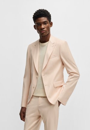 Pale pink suit with two buttons, notched lapel, and side pockets. Worn over a light beige sweater, smooth fabric and fitted design.