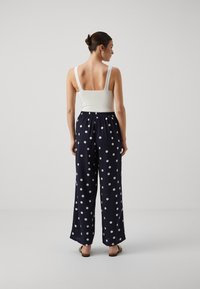 Hvitt tanktopp og marineblå bukser med prikkete mønster og elastisk midje. Glatt stoff og ankel-lengde design. Enkle sandaler.