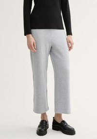 Pantalones de pierna amplia en gris, fabricados en un tejido suave con una textura lisa, combinados con zapatos negros sin cordones con una suela gruesa.