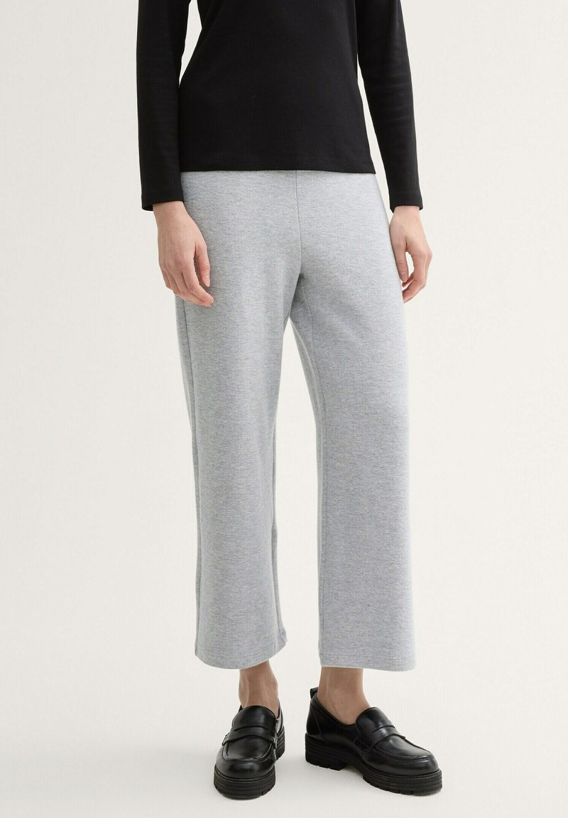 Pantalones de pierna amplia en gris, fabricados en un tejido suave con una textura lisa, combinados con zapatos negros sin cordones con una suela gruesa.