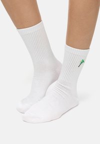 Calcetines de algodón blancos de caña corta con textura acanalada y bordado de una palmera verde en el lado exterior.