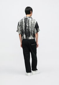 Kurzärmliges Hemd in schwarz-weißem abstraktem Muster, kombiniert mit schwarzen Jogginghosen mit kleinem Logo auf der Gesäßtasche. Weiße Turnschuhe.