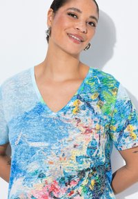 T-shirt z dekoltem w kształcie litery V w jasnoniebieskim kolorze z abstrakcyjnymi, kolorowymi wzorami kwiatowymi, wykonany z miękkiego materiału i o luźnym kroju.