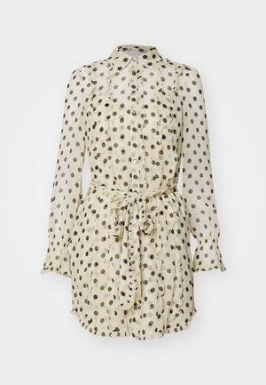 Bluză crem transparentă cu buline negre, cu un front volă, închidere cu nasturi și talie legată. Are mâneci lungi cu manșete volan.