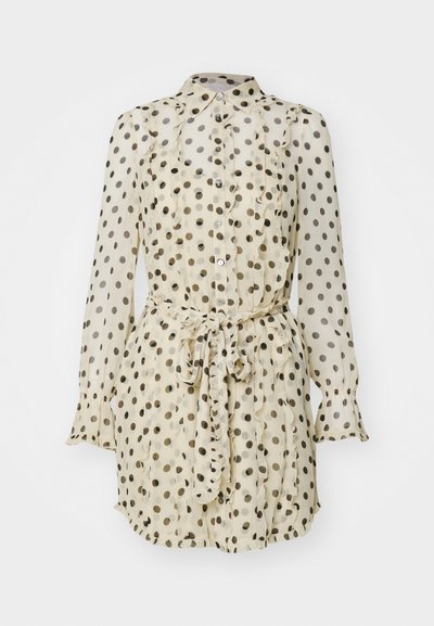 Häikäisevä kermanvärinen paita mustilla pilkuilla, rypytetty etuosa, nappikiinnitys ja nauhavyötärö. Ominaisuuksiin kuuluvat pitkät hihat frillattujen hihansuiden kanssa.