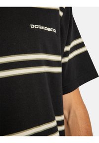 Camiseta a rayas negra con rayas horizontales verdes y blancas, hecha de suave algodón, con un logo en el pecho.