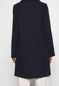 Marineblauer Mantel aus strukturiertem Stoff, mit langen Ärmeln und Rückenschlitz. Verfügt über einen Kragen und ein gerades Schnittdesign.