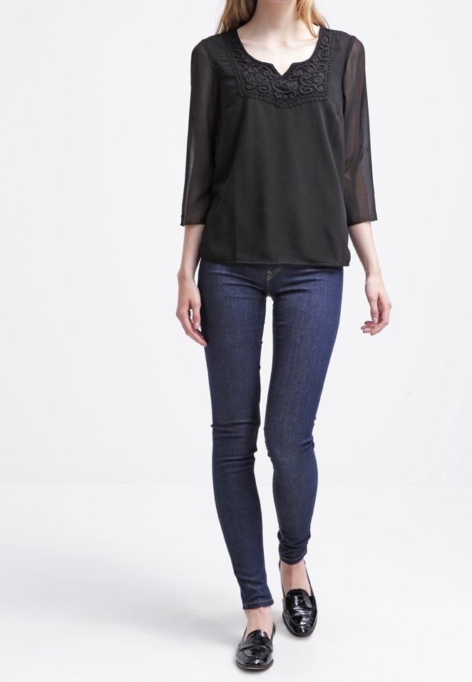 Czarna przezroczysta bluzka z haftem kwiatowym przy dekolcie, w połączeniu z ciemnoniebieskimi wąskimi dżinsami i czarnymi mokasynami.