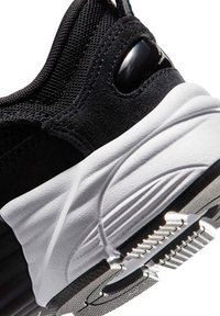 Talons de baskets noirs avec semelle blanche texturée et bande de roulement, avec tissu en mesh et superpositions en daim, montrant une partie d'un panneau de logo brillant.