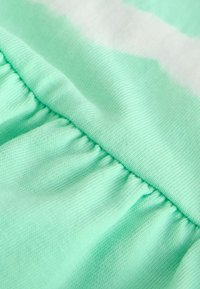 Gros plan sur un tissu vert menthe avec une ceinture élastique froncée et un motif subtil tie-dye blanc sur une matière douce en coton.