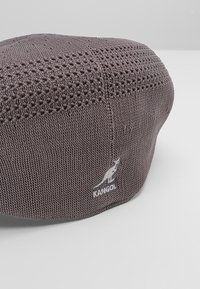 Šedá pletená beretová čepice s texturovaným vzorem, vyšívaným logem Kangol a zaobleným tvarem. Vyrobena z pružného, prodyšného materiálu.