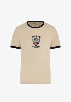 T-shirt beige in cotone con collo e polsini a costine blu navy, presenta logo ricamato e stemma sul petto, testo recita "G.U.E.S.S. ATHLETIC DIVISION."