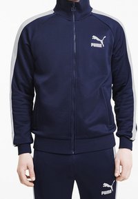 Námořnická sportovní bunda s vysokým límcem, plným zipem a šedými bočními akcenty. Vyrobena z hladkého materiálu s logem na hrudi.