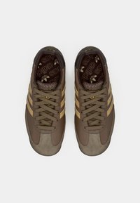 Smeđe tenisice s bež detaljima, imaju teksturirani ante na prstu, mrežasti jezik i tri vodoravne pruge sa strane.