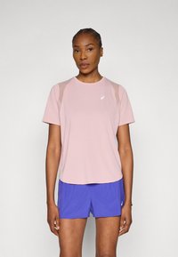 Ροζ αθλητική μπλούζα με κοντά μανίκια, στρογγυλή λαιμόκοψη και διακοσμητικά από δίχτυ. Συνδυάζεται με μπλε σορτς, που φέρουν λογότυπο στο κάτω αριστερό μέρος.