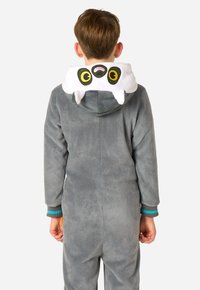 Sivý flísový overal s kapucňou, na ktorej je biely dizajn zvieracej tváre, veľké žlté oči a malé tesáky. Manžety majú teal pruhy.