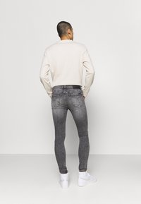 Jeans de denim gris ajustados con una textura desgastada y bolsillos traseros, combinados con una camisa de manga larga ligera y zapatillas blancas.