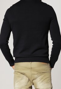 Granatowy sweter z okrągłym dekoltem, z długimi rękawami, ściągaczami przy mankietach i u dołu; zestawiony z jasnymi, fakturowanymi chinosami z tylnymi kieszeniami.