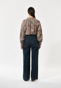 Blusa con stampa floreale, colletto arricciato e maniche lunghe, abbinata a jeans in denim scuro a vita alta e gamba larga con tasche posteriori.