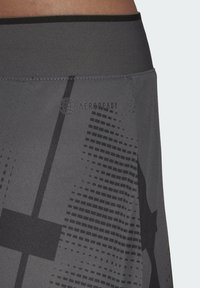 Grå sportkjol med AeroReady-logotyp, mönstrad textur med prickiga och blockmönster, samt en kontrasterande svart midja.