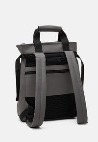 Mochila gris con una carcasa suave y estructurada. Cuenta con un panel de malla, correas de hombro acolchadas y asas superiores. Diseño sencillo y funcional.