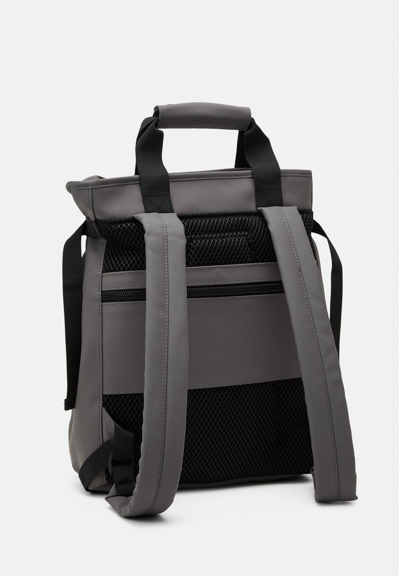 Zaino grigio con una struttura a guscio morbido. Presenta un pannello in rete, spallacci imbottiti e manici superiori. Design semplice e funzionale.