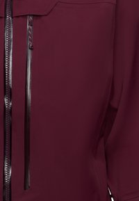 Vinröd jacka med en elegant design, två parallella dragkedjefickor med strukturerade detaljer och en mjuk tygkänsla.