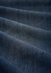 Denimová tkanina v hlubokém modrém odstínu s viditelnou texturou, diagonálními záhyby a jemným třepením, která ukazuje svůj tkaný vzor a hmotnost.