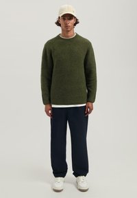 Groen gemêleerd trui met een ronde hals, over een wit shirt gedragen, gecombineerd met navy losvallende broeken en witte sneakers.