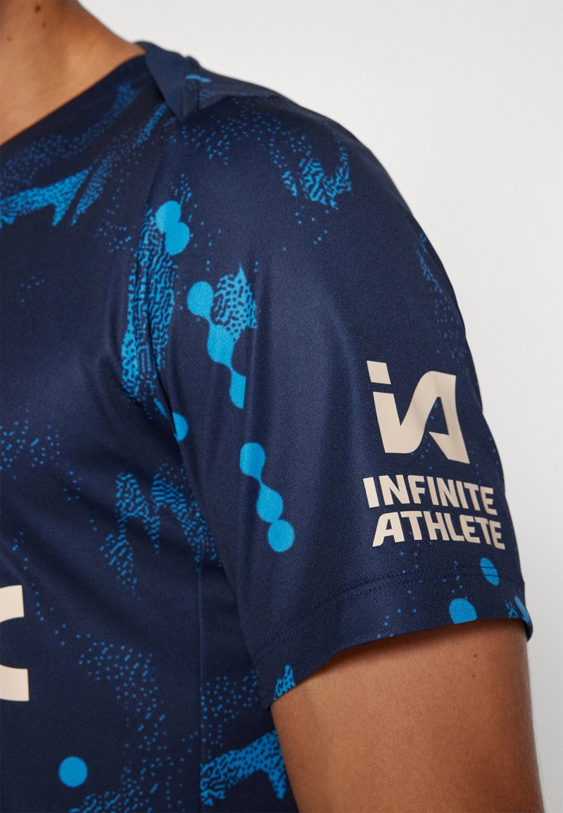 Maglietta sportiva a maniche corte di colore blu navy, con un motivo astratto blu e un logo crema che recita “INFINITE ATHLETE” sulla manica.