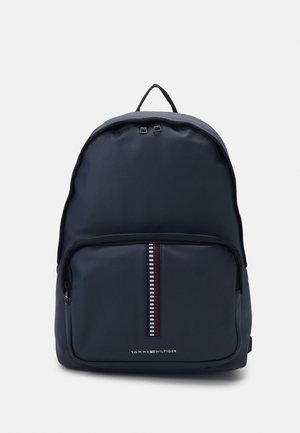 Navy blue backpack made of smooth fabric with a front zip pocket featuring a patterned stripe. It has a top loop and logo at the bottom.