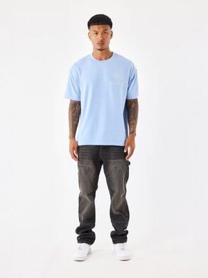T-shirt bleu clair à manches courtes avec un petit graphisme sur la poitrine, associé à un pantalon cargo noir délavé et des baskets blanches.