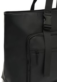Černá taška přes rameno vyrobená z hladkého, matného materiálu. Obsahuje přední kapsu na zip a nastavitelné ramínko. Jednoduchý, moderní design bez zdobení.