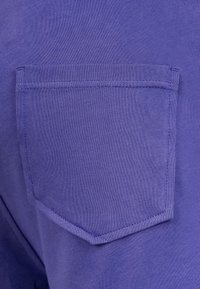 Tessuto di cotone viola con una tasca a toppa di forma rettangolare, bordi cuciti con cura e una texture liscia.