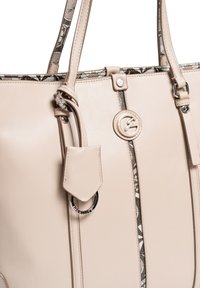 Beżowa skórzana torba na ramię z dwoma wytrzymałymi uchwytami, z wzorzystą podszewką i srebrnym pierścieniem jako ozdobą na bocznej zawieszce.