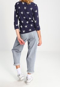 Laivastonsininen pitkähihainen paita, jossa on valkoinen meritähtikuosi, yhdistettynä vaaleansinisiin raidallisiin, löysästi istuviin housuihin ja valkoisiin tennareihin, joissa on käännetyt lahkeet.